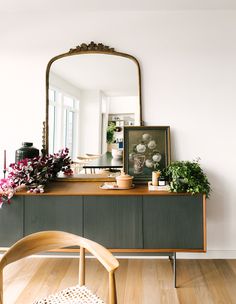 a wooden table topped with flowers next to a large mirror and a plant on top of it