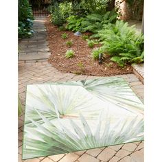 a green and white area rug sitting on top of a brick walkway next to trees