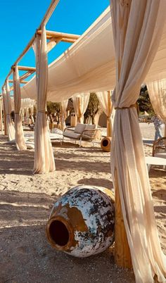 an outdoor area with white drapes and chairs on the sand, covered by curtains