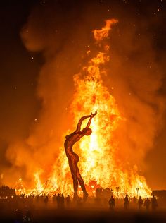 a woman standing in front of a huge fire with her arms up and legs spread out