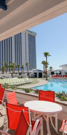 red and white chairs sitting on top of a balcony next to a swimming pool with a hotel in the background