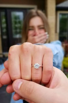 a woman is holding her engagement ring in front of the camera while another person looks on