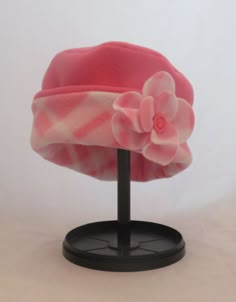 a pink and white hat with flowers on it sitting on a black stand against a white background