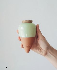 a hand holding a small green vase with a cork top on it's tip