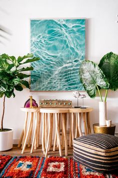 a living room with some plants on the table and a large painting above it,