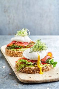 two sandwiches with cheese, lettuce and tomato on them sitting on a cutting board