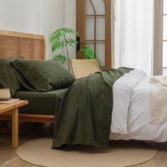 a bed with green sheets and pillows in a room next to a window, near a coffee table