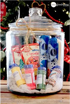 a glass jar filled with lots of different types of condiments and candy in front of a christmas tree