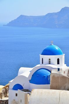 a blue and white church on top of a hill near the ocean with mountains in the background