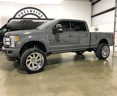 a large gray truck parked in a garage next to two other trucks with chrome rims