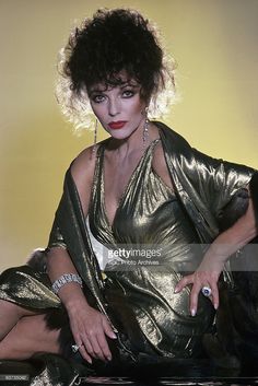 a woman in gold dress sitting on the floor with her hand on her hip and looking at the camera