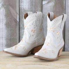 a pair of white cowboy boots sitting on top of a wooden table