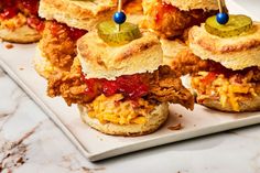 several mini sandwiches with pickles on them sitting on a white plate next to a marble counter