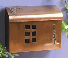 a house shaped mailbox mounted to the side of a purple wall next to a potted plant