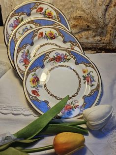 four plates with flowers on them sitting next to tulips