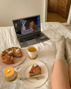 a laptop computer sitting on top of a bed next to two slices of pie and a cup of tea