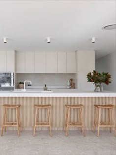 three wooden stools sit in front of a kitchen island with an oven and microwave