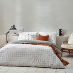 a bed sitting next to a chair and lamp on top of a wooden floor in a bedroom