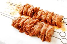 several skewers of meat sitting on top of a white surface with gravy