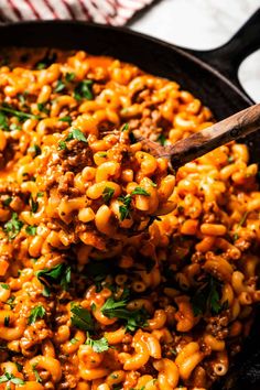 a skillet full of macaroni and cheese with a wooden spoon in it