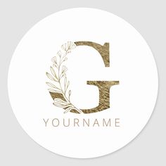 the letter g with an olive branch and leaves in gold on a white round sticker