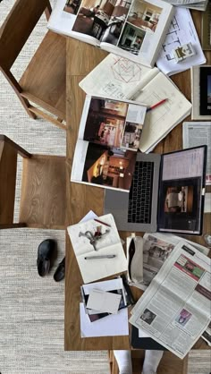 a wooden table topped with lots of papers and laptop computer sitting on top of it