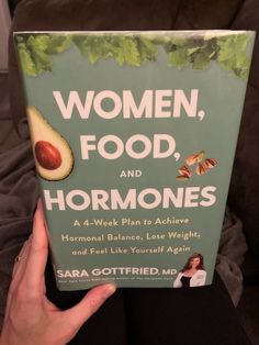 a person holding up a book about women, food and hormonies with an avocado on the cover