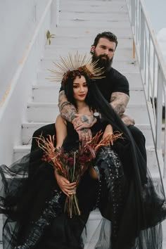 a man and woman dressed in black sitting on the steps with their arms around each other