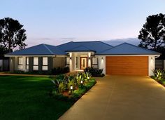 a modern house is lit up at night with lights on the front door and driveway