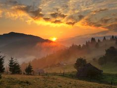 the sun is setting in the mountains with trees and grass on the hillside below it