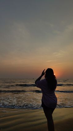 a woman standing on top of a sandy beach next to the ocean at sun set