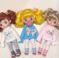 three dolls with blonde hair are laying next to each other on a white surface,