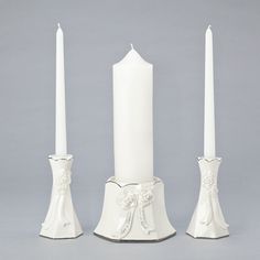 three white candles are sitting next to each other on a gray surface with one candle in the middle