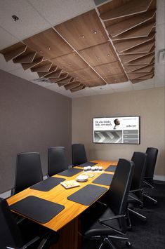 a conference room with black chairs and a wooden table in front of a flat screen tv