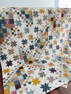 a quilt made with multi colored stars on a wooden floor in front of a window