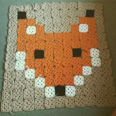 an orange and white crocheted square with black squares on it, sitting on a table