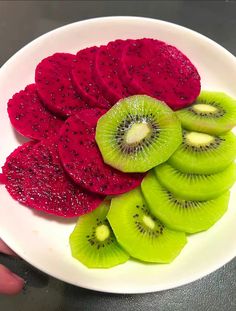 a white plate topped with sliced kiwis and raspberries on top of each other