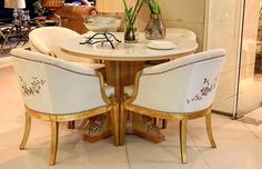 two white chairs sitting at a round table with gold trimmings on the legs