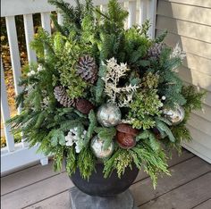 a potted plant with evergreen, pine cones and other greenery on a porch