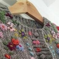 a close up of a sweater with flowers on it and a wooden hanger in the background