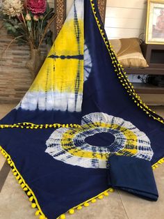 a blue and yellow tie - dyed blanket sitting on the floor next to a vase with flowers