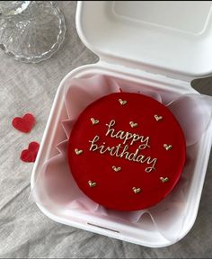 a red birthday cake in a white box with hearts on the table next to it