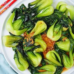 a white plate topped with green vegetables next to chopsticks on a blue table cloth