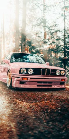 a pink car parked on the side of a road in front of some tall trees