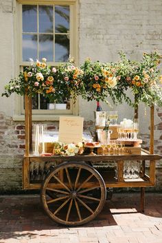 a wooden cart with flowers and wine glasses on it sitting in front of a brick building