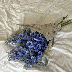 a bouquet of blue flowers laying on top of a white sheet covered bed next to a newspaper