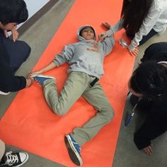 a man laying on top of an orange mat with people around him looking at him