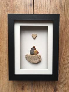 there is a small rock with a heart on it in a black shadow box frame