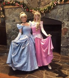 two women dressed up as princesses standing next to each other in front of a fireplace