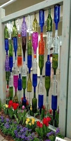 there are many different colored wine bottles hanging on the side of a wall with flowers in it